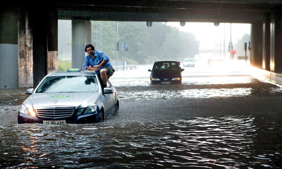 En taxachauffør på vej ud af sin vogn i København under et voldsomt skybrud i juli 2011. Det var den vejrepisode, der for alvor satte skub i interessen for permeable belægninger i Danmark. Men selvom flere kommuner har vist interesse for permeabel asfalt og anden belægning, er det et fåtal af dem, der har gjort alvor af interessen.